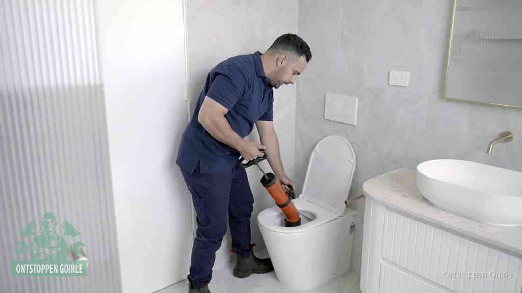 Een monteur buigt over een wandcloset en duwt met de hand een persluchtontstopper in de toiletpot om de verstopping handmatig los te maken in Goirle