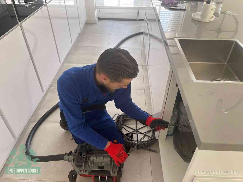 Een monteur ontstopt de keukenafvoer onder de spoelbak met een elektrische veermachine in Goirle
