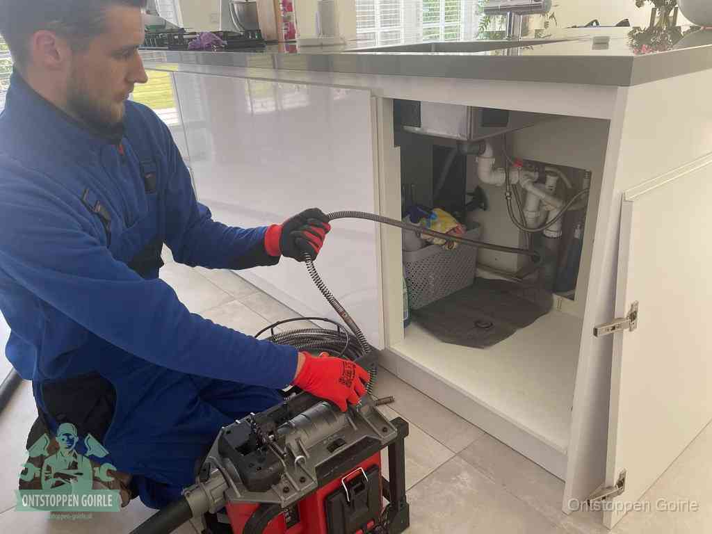 Monteur voert een ontstoppingsveer in de afvoer onder de keuken in Goirle