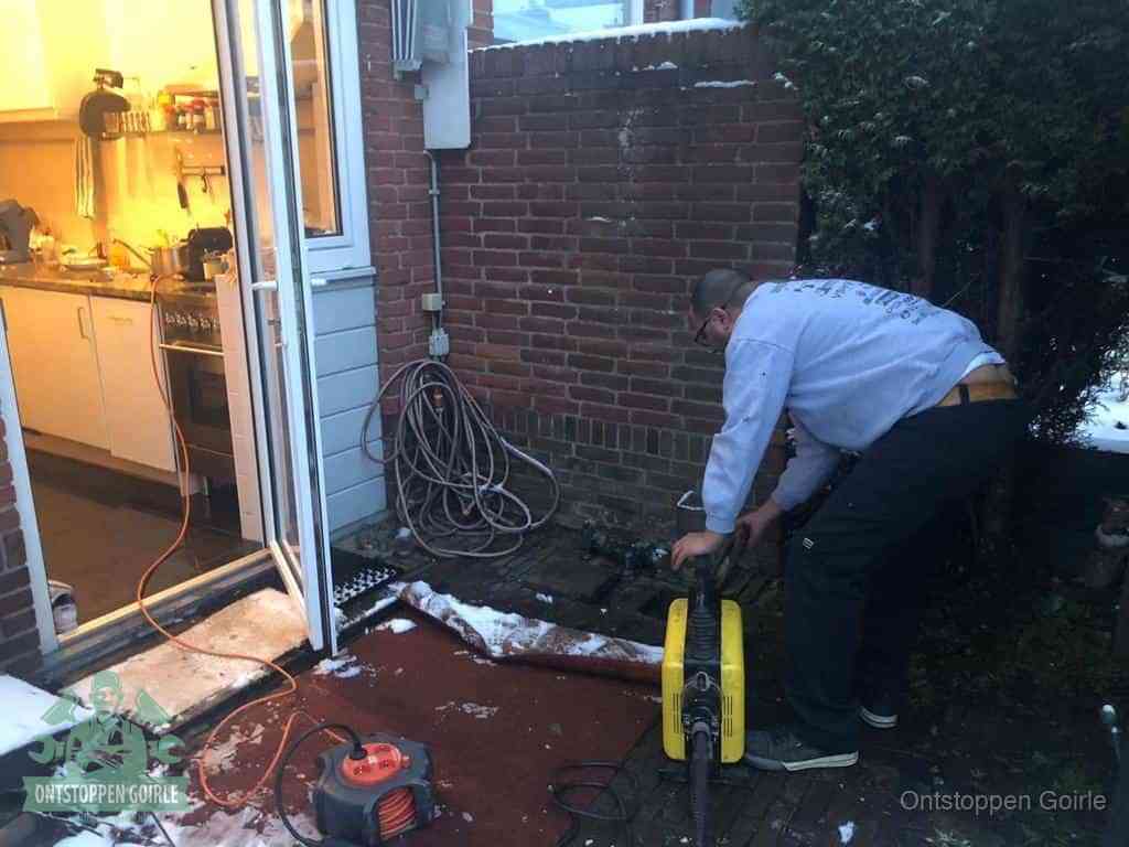 Een monteur werkt buiten bij een open riool-/grondput met een elektrische ontstoppingsmachine om een verborgen afvoerprobleem op te sporen in Goirle