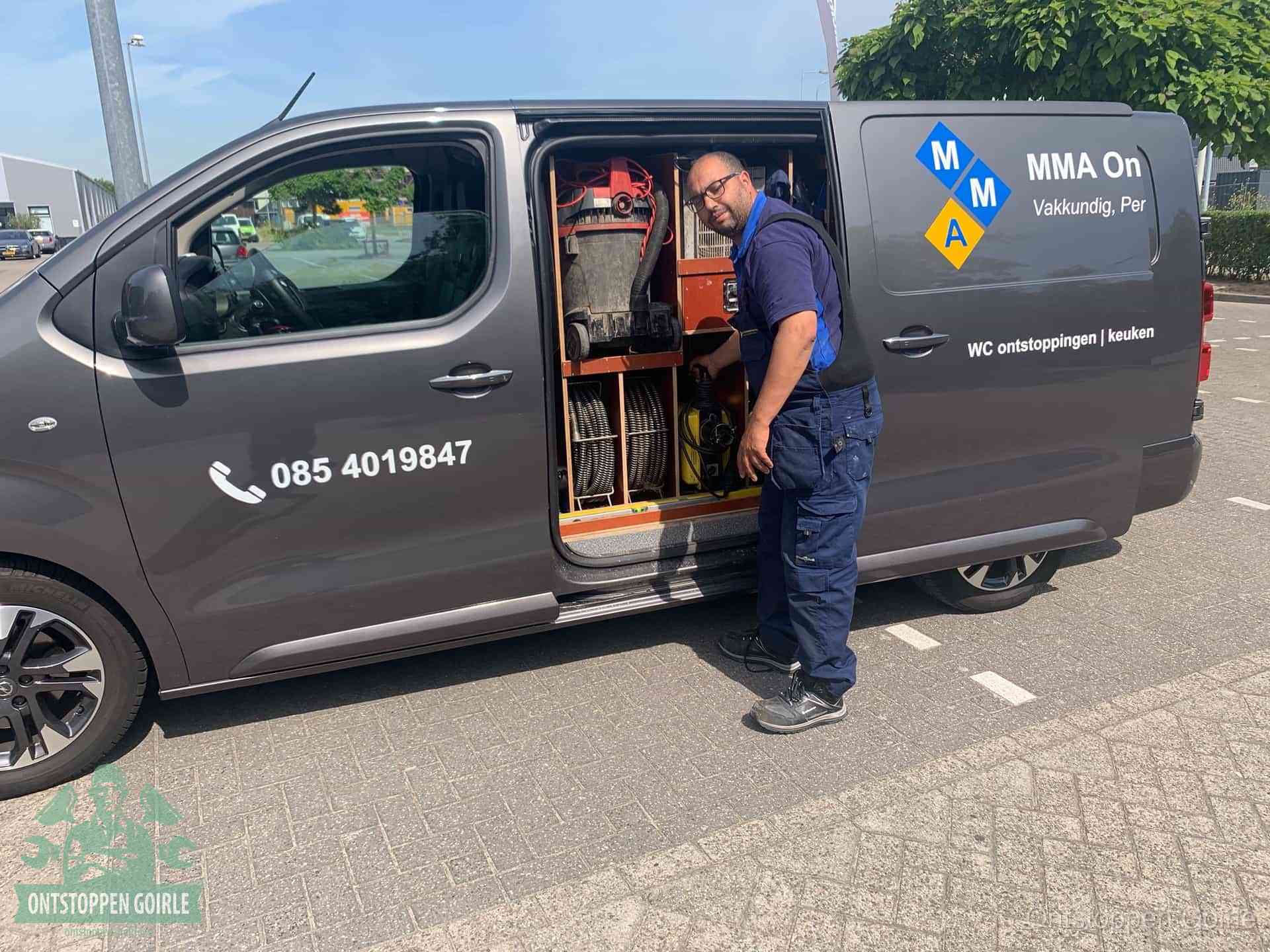 Een monteur bij de open schuifdeur van zijn bedrijfsbus op een parkeerplaats, klaar om de oorzaak van terugkerende afvoerverstoppingen aan te pakken in Goirle