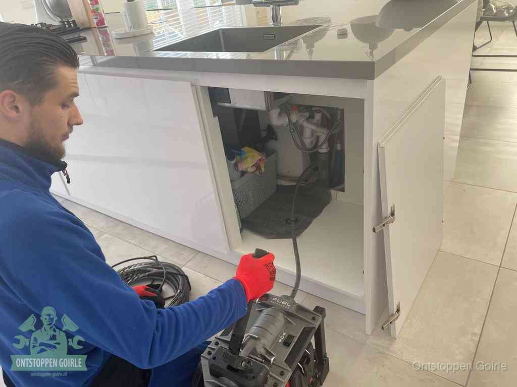 Monteur ontstopt met een veermachine een verstopte afvoer onder de gootsteen in Goirle