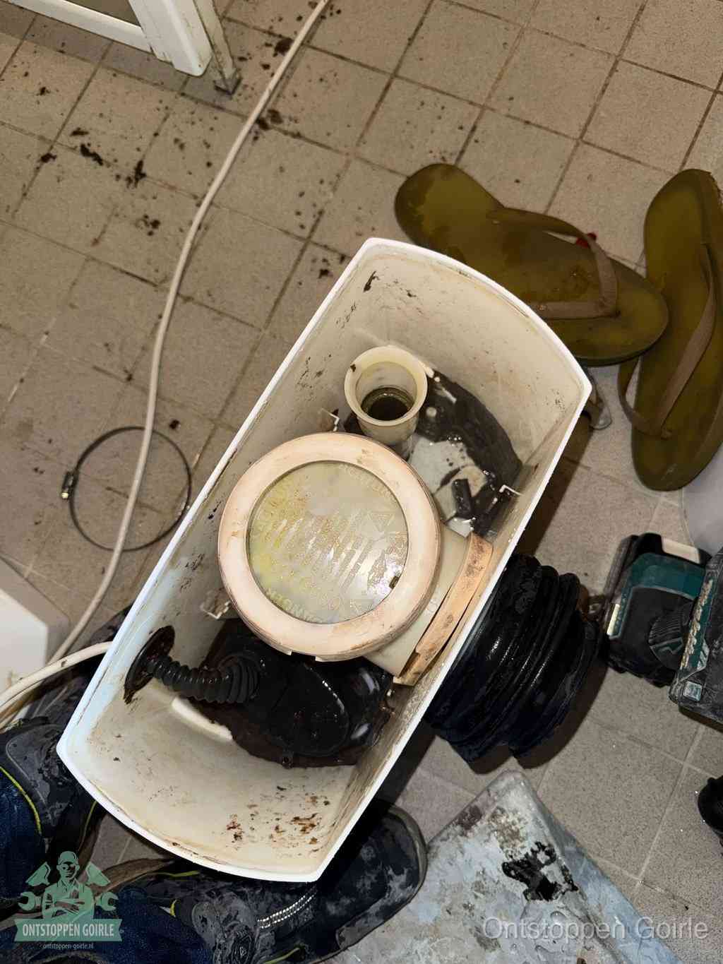 Een gedemonteerde toiletpot op de vloer met ontstoppingsveer en gereedschap ernaast, het verwijderen van een vastzittend voorwerp uit de wc in Goirle