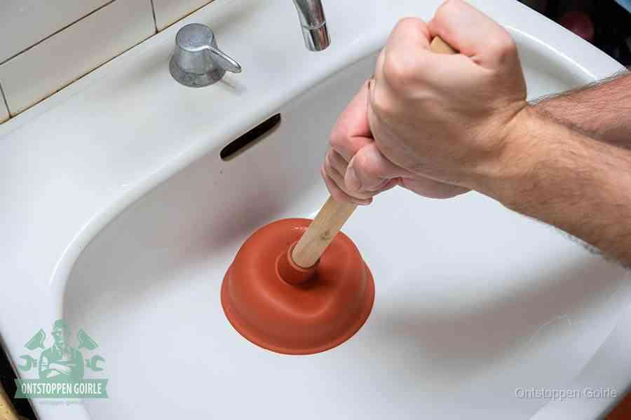 Twee handen gebruiken een rode rubberen plopper op een sanitair-afvoer om het toilet te ontstoppen in Goirle