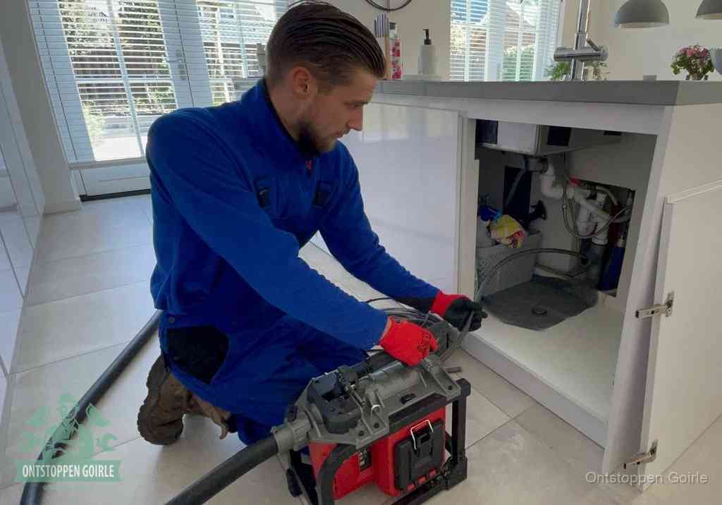 Een monteur voert een professionele elektrische ontstoppingsmachine in de afvoer onder de spoelbak tijdens het gootsteen ontstoppen in Goirle