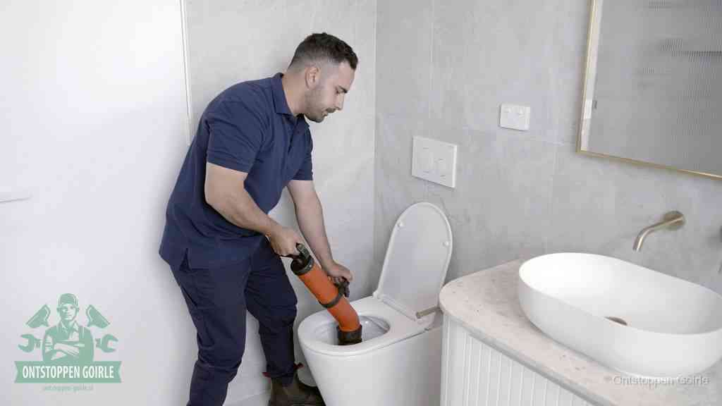 Een man gebruikt een handmatige luchtdruk-ontstopper in een modern betegeld toilet om zelf de wc te ontstoppen in Goirle